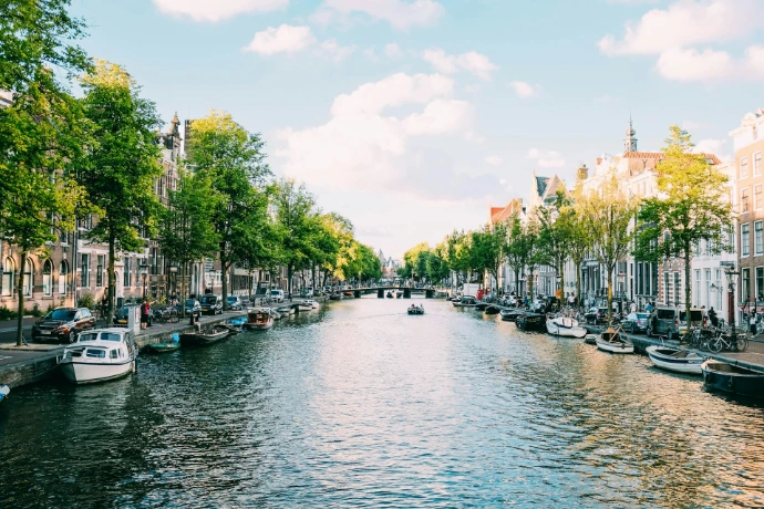 Boats moored along a canal lined with trees and historic buildings in Amsterdam